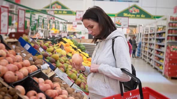 Midrange Caucasian Woman in a White Sweater in a Shopping Mall with Fruits in a Supermarket Buys a alt