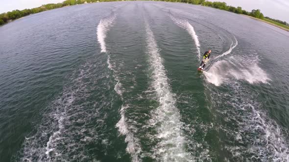 Aerial birds-eye drone view of a man wakeboarding behind a boat. alt