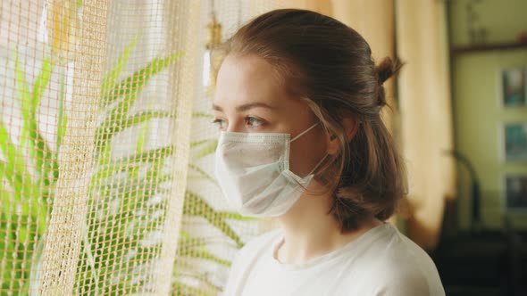 Young Student Teenager Girl in Protective Mask Standing Near Window on Home Self Isolation alt