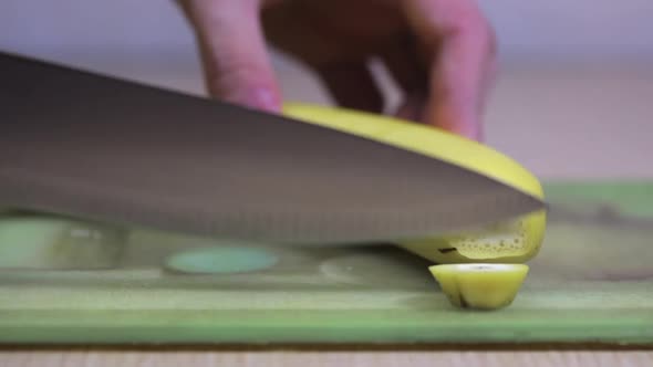 A Man's Hand Cuts a Banana on the Table with a Knife