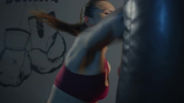 A boxer girl in a red tracksuit hits a punching bag