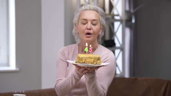Portrait of Happy Confident Beautiful Caucasian Woman Blowing Out Candles on 45 Birthday Smiling alt