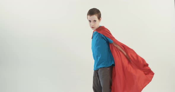 Boy with a superhero cape pretends to fly on a white studio background alt