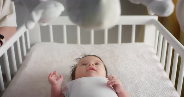 Newborn Baby in a White Bodysuit is Lying on His Back in a Light Child Crib