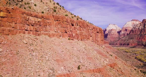 A drone flies past a rock wall to reveal a glorious valley and mountain range beyond. alt