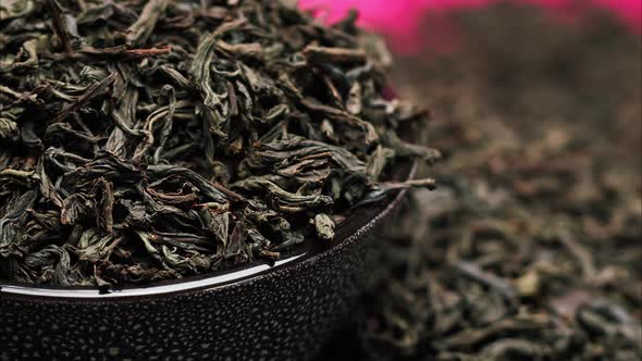 Closeup of Falling Down Dried Tea Leaves Into Black Bowl on Pink Background alt