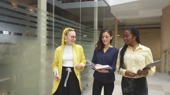 Three Beautiful Business Women Walking in the Office and Discussing Project alt