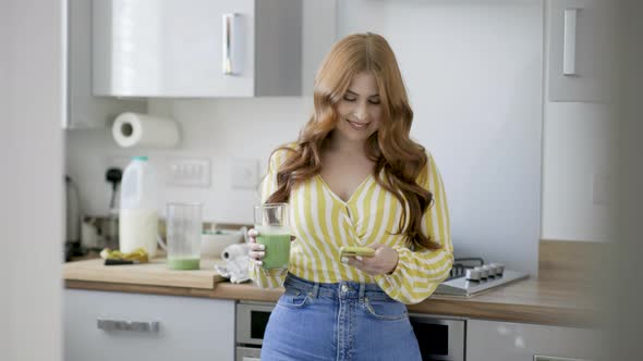 Young woman checking smartphone while holding green smoothie