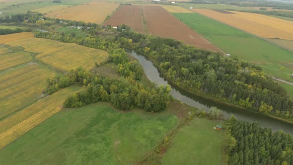 Rural farmlands with river running through and trees growing on each edge alt
