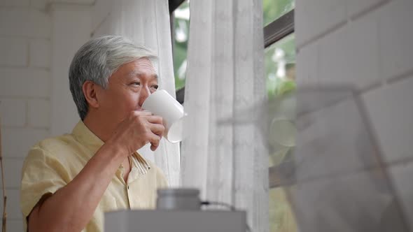 Portrait senior Asian man drinking tea morning beside a window at home.