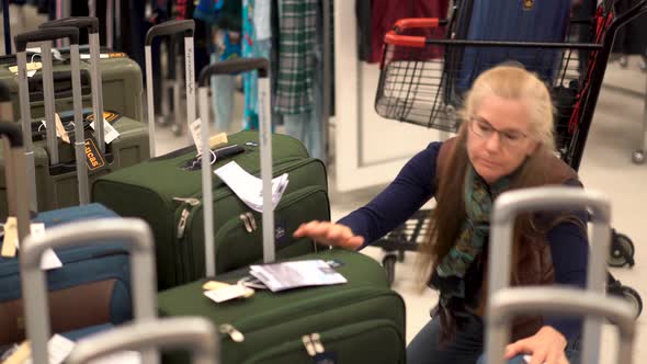 Blonde woman looking for carry on luggage in a hypermarket. alt