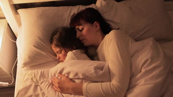 Mother Hugs Her Cute Kid Daughter While Sleeping Together in Bed in Cozy Bedroom alt