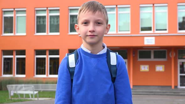 A Young Boy Applauds To the Camera - an Elementary School in the Background alt