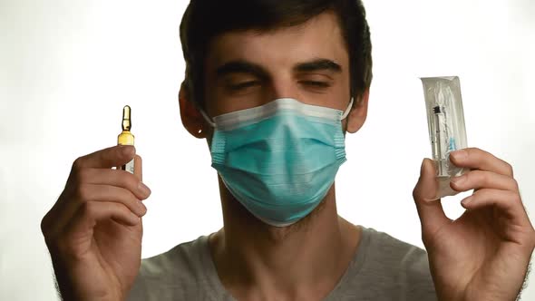 Portrait of a Young Man in Medical Mask Looks at the Vial and Syringe on a White Background