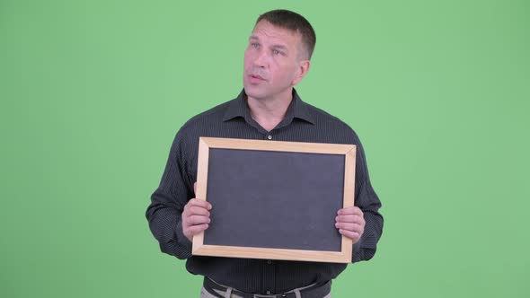 Macho Mature Businessman Talking While Holding Blackboard alt