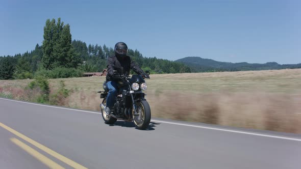 Tracking shot of man riding motorcycle on country road.  Fully released for commercial use.