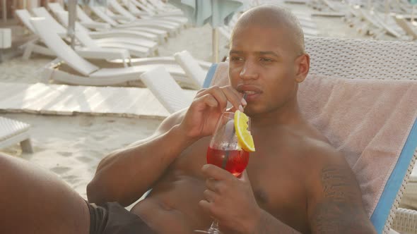 Handsome African Man Drinking Cocktail While Relaxing at the Beach alt