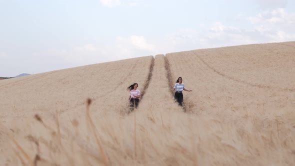 Two young female friends enjoying the nature together while walking in a wheat field. alt