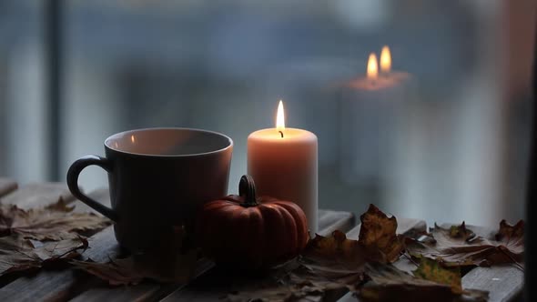 Candle, leaves and cup f coffee on wooden table.