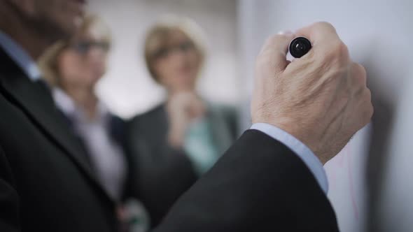 Senior Businessman Talking to Younger Colleagues and Writing on Board, Planning alt