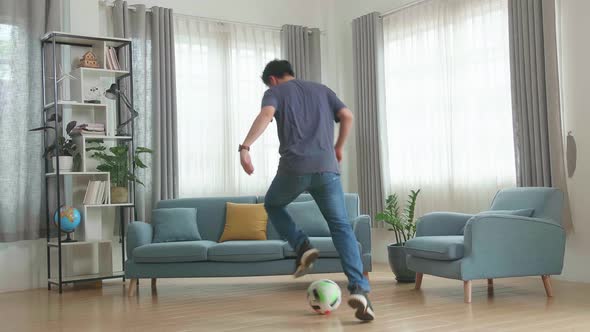 Asian Man Playing Soccer Ball In Living Room alt