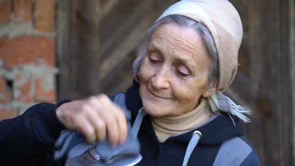 Happy Beautiful Senior Woman is Holding Metal Hoe and Making It Clean After Work and Weeding in the alt