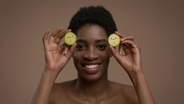 African Lady Posing With Cucumber Slices Covering Eyes Beige Background alt