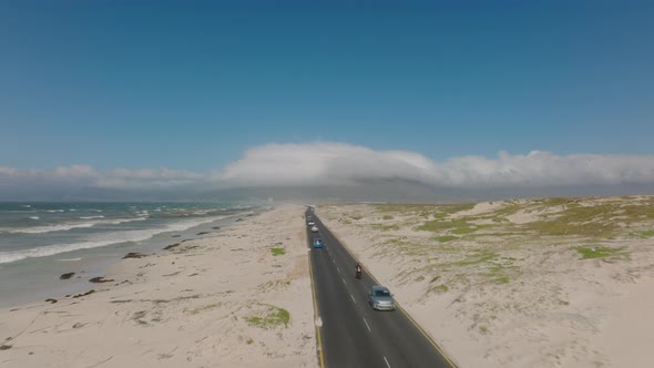 Aerial View of Traffic on Road Leading Through Sand Field Along Sea Coast alt