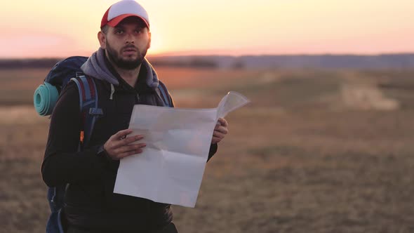 Adventure Man with Map and Extreme Explorer Gear on Mountain with Sunset alt