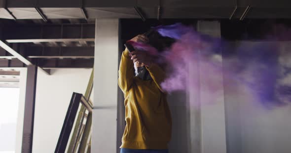 Mixed race woman holding blue and purple flares standing in an empty building alt