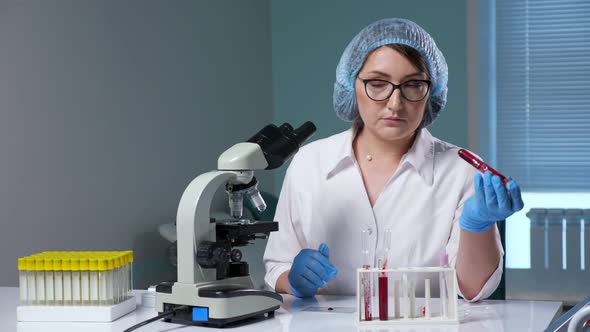 Woman Checks Blood Sample in Test Tubes in Laboratory alt