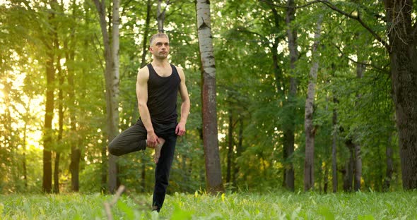 Young Man Practicing Yoga Lesson Inside a Park in the Morning alt