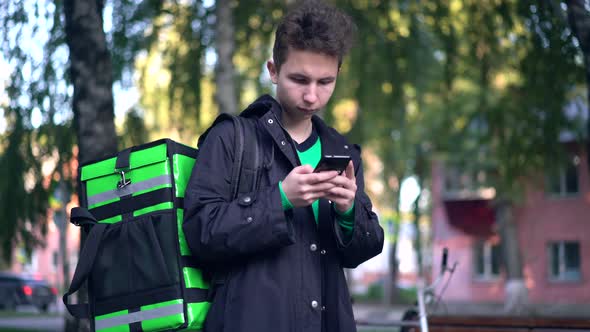 Delivery Man with Green Backpack Awaiting the Order for Delivery alt