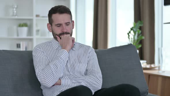 Pensive Young Businessman Sitting on Sofa and Thinking at Home  alt