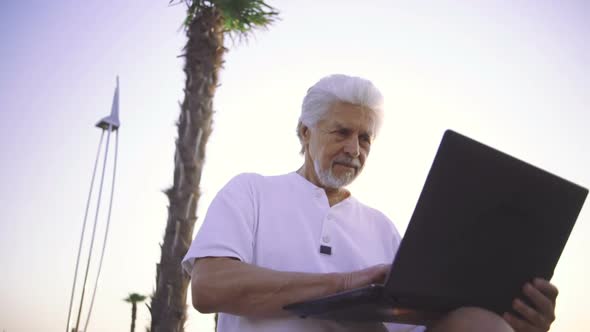 Portrait of Retirement Handsome Senior Man Using Laptop Computer on Seafront alt