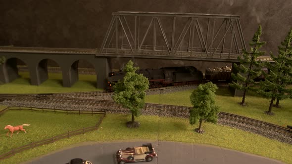 Toy Freight Train Moving on Railroad Under the Bridge. alt