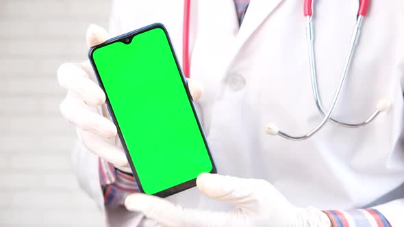 Doctor's Hand in Protective Gloves Holding Smart Phone with Green Screen alt