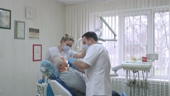 Dentist with Assistant in Protective Masks Working with Patient in Dental Clinic alt