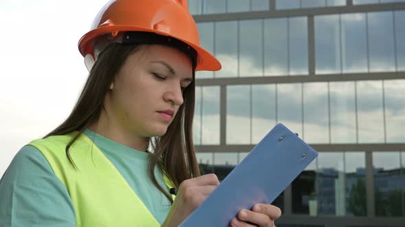 Young Female Builder in a Signal Vest and Helmet Writes Something alt