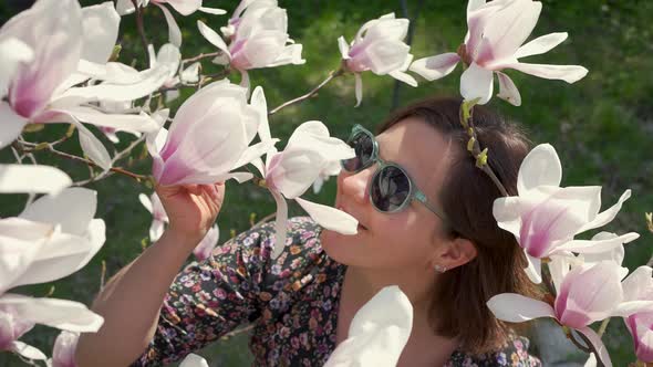 Happy Woman Enjoying Nature and Touching Blooming Magnolia Flowers in the Garden