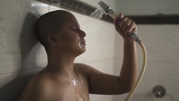 Sick and tired bald Indian girl is bathing with hand shower in bathroom is very upset,  cries and br alt
