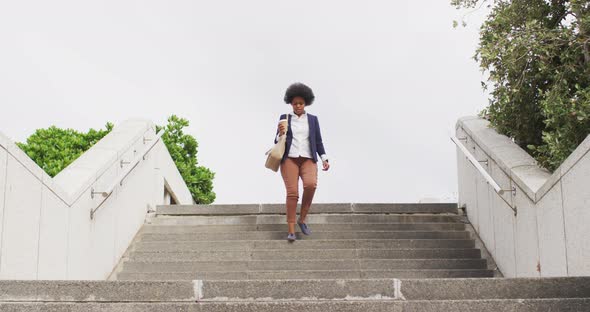 African american businesswoman holding takeaway coffee and walking alt