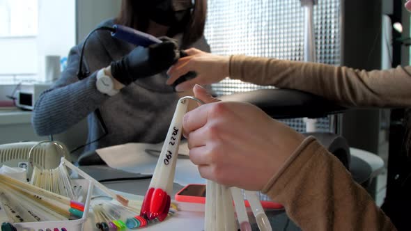 Beauty Salon Visitor Looks at Palette with Coloured Manicure alt