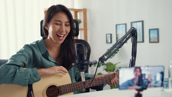 Asia girl influencer play guitar music use microphone record with smartphone for online audience.