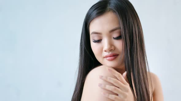 Medium Closeup Portrait of Pretty Asian Woman Flirting and Smiling Touching Naked Shoulder By Hand alt