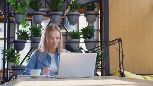 Female Blogger Sitting at Cafe with Laptop and Microphone alt