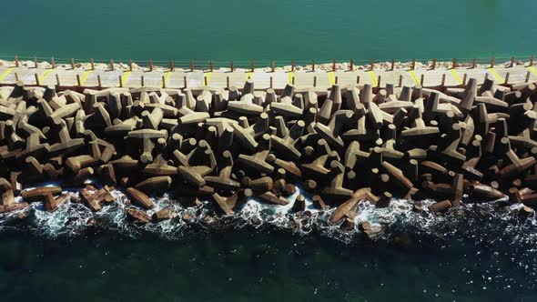Small blue waves from the clear Mediterranean sea splash on the man-made pier with large unusually s alt