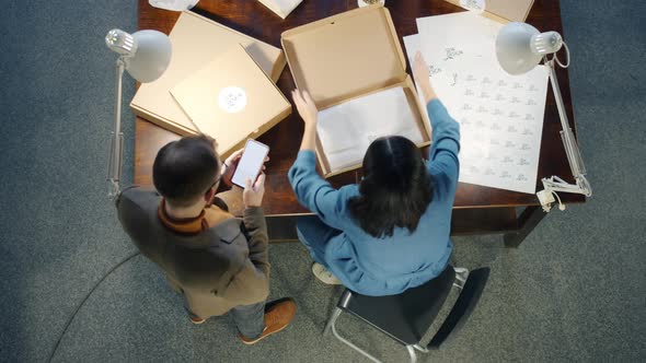 Top View of Business Partners Packing Handmade Garments in Cardboard Boxes Working in Studio alt