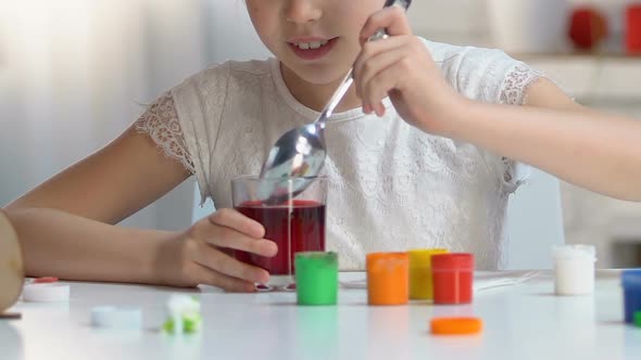 Excited Girl Taking Colored Egg From Glass With Red Food Coloring alt