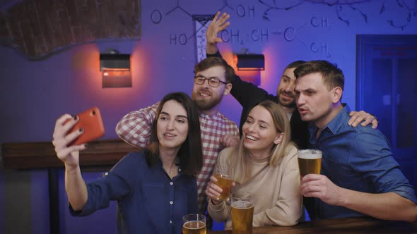 Friends in Pub on Bar Counter with Beer Glasses in Hands Make Group Selfie